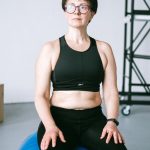 Middle-aged woman with eyeglasses exercising on a blue stability ball indoors.